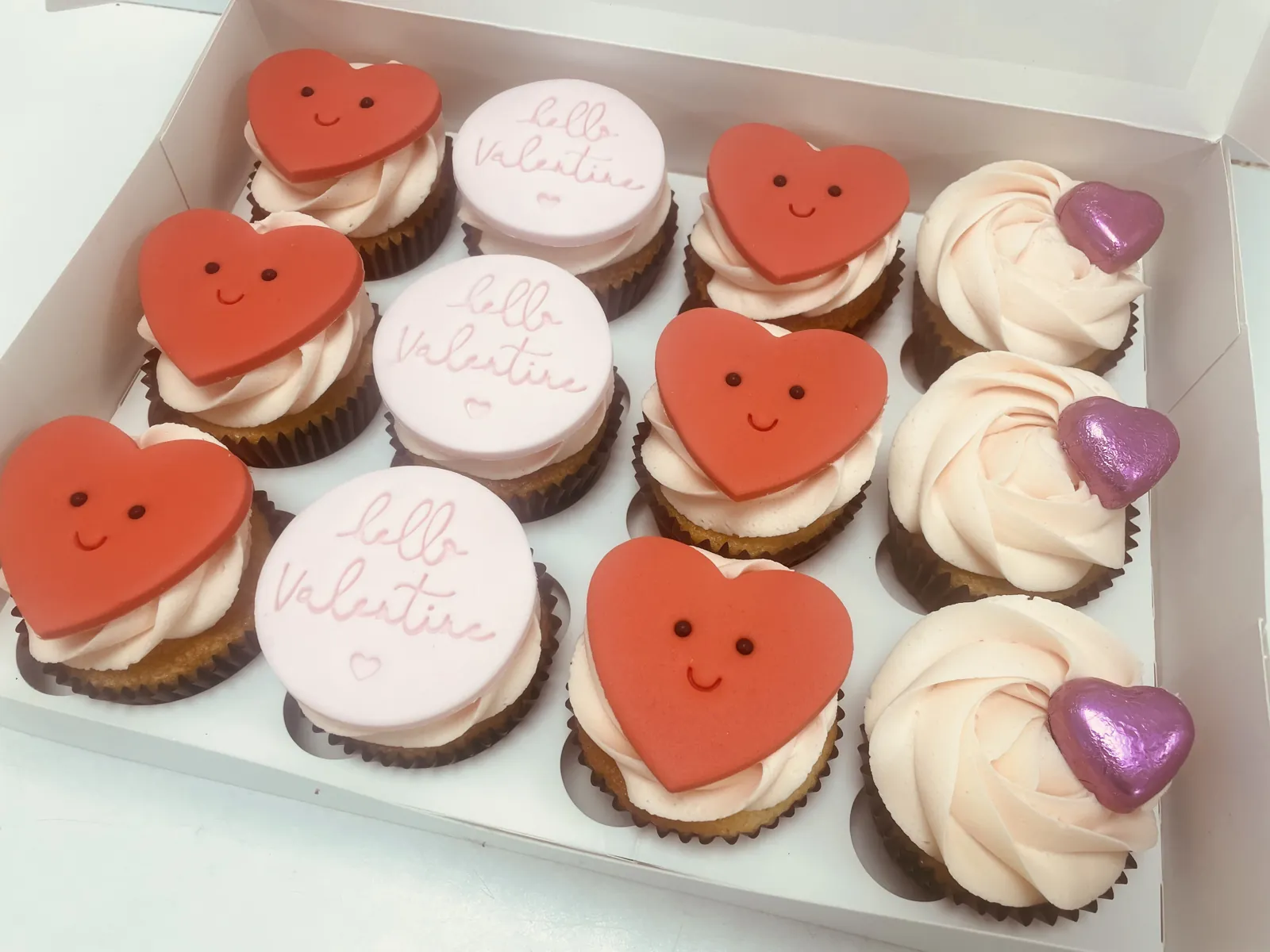 Box of Valentine cupcakes with red heart toppers and buttercream swirls